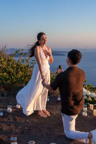 Emotional sunset marriage proposal with candles and white roses above the Santorini caldera